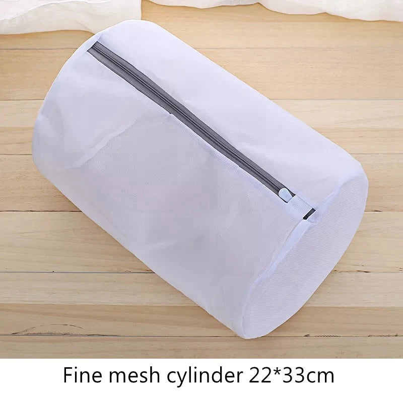 Bolsa de ropa cilíndrica de malla fina blanca con cremallera sobre una superficie de madera.