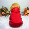 A bright red hoodie with a gold fluffy hood rests on a white surface surrounded by dried flowers and greenery.