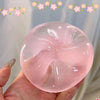 Eine Hand hält eine durchscheinende rosa Stressball-Kugel mit Blumenmuster vor einem hellen Hintergrund.