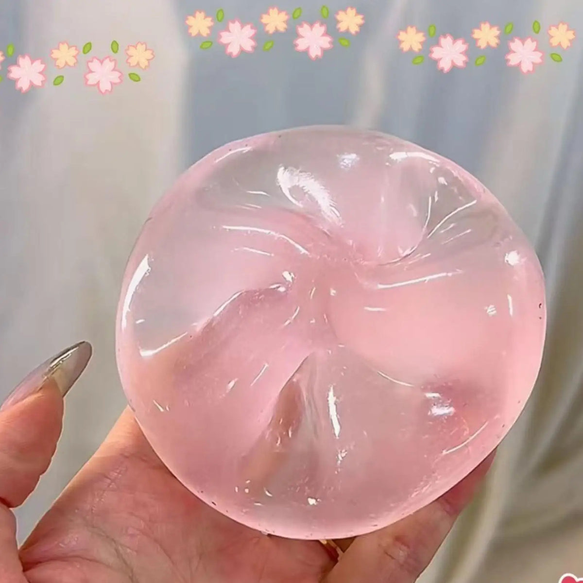 Eine Hand hält eine durchscheinende rosa Stressball-Kugel mit Blumenmuster vor einem hellen Hintergrund.