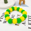 A circular collar made of fluffy green and yellow pom-poms, resembling flowers, displayed on a white surface.
