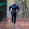 A man is running a dog on a leash with a waist bag in a forest setting.