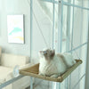 A white cat is resting in an aerial hammock pet bed inside a glass enclosure.
