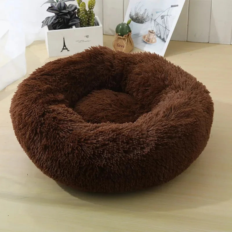 A round, dark brown plush faux fur bed for cats and dogs resting on a light wooden surface.