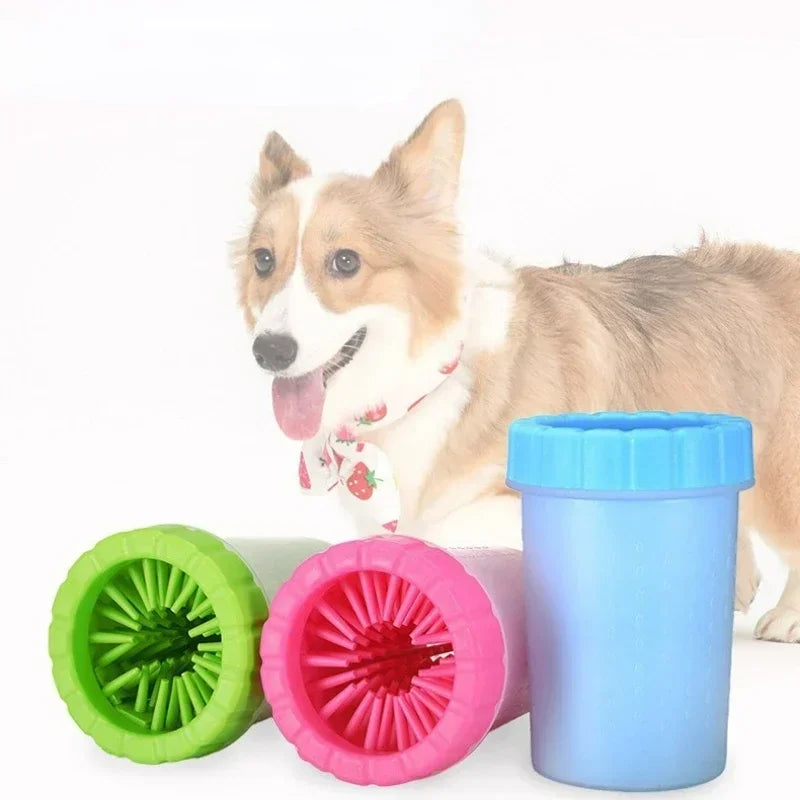 A fluffy dog is sitting next to a blue silicone pet paw cleaner and pink silicone cleaning tools.