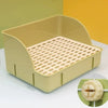 Una caja de arena rejillada amarilla clara y desmontable para pequeños mamíferos, mostrada sobre una superficie blanca.