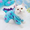A white kitten wearing a bright blue fleece hoodie with purple polka dots, lying on a white surface.