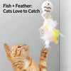 A tabby kitten is looking up at a feather and fish toy designed for cats to catch.