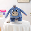 A blue flannel hoodie shaped like a donkey is worn by a white dog sitting on a white table.