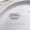 Pink bow hair accessory featuring pearl accents and rhinestones placed on a white plate.