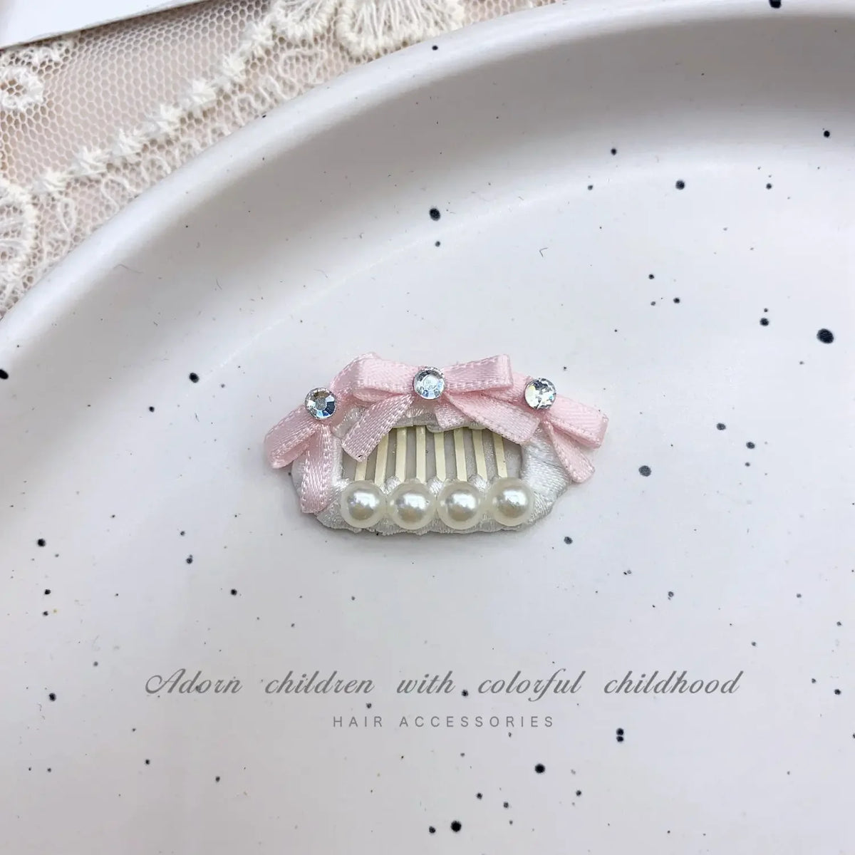 Pink bow hair accessory featuring pearl accents and rhinestones placed on a white plate.
