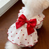A white pet dress with red polka dots and a large red bow, featuring a leash ring detail.