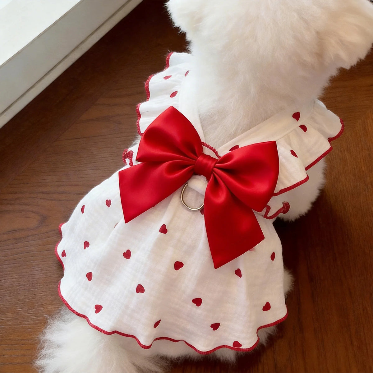 A white pet dress with red polka dots and a large red bow, featuring a leash ring detail.