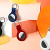 Various silicone airtag protective covers in black, blue, red, and white with metal keychains displayed on a light background