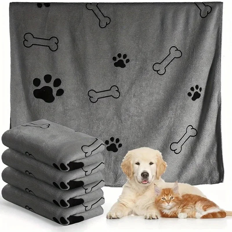 A gray pet bath towel with paw print and bone patterns is shown alongside a stack of towels and a cat and dog.