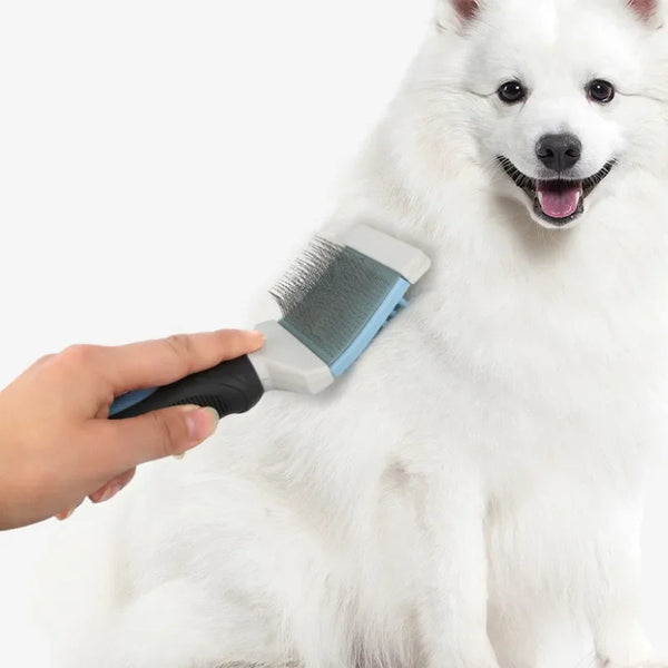 A hand is using a double-sided grooming comb with massage bristles on a white dog's fur.