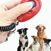 Eine Hand hält einen roten, verstellbaren Hundetrainer-Klicker, während mehrere Hunde in die Kamera schauen.