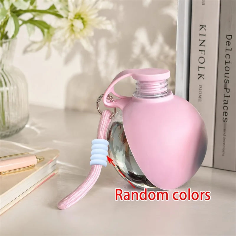 A pink portable pet water bottle with a lanyard is shown next to a stack of books.