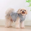 A light tan dog wearing a gray fleece hoodie, standing indoors.
