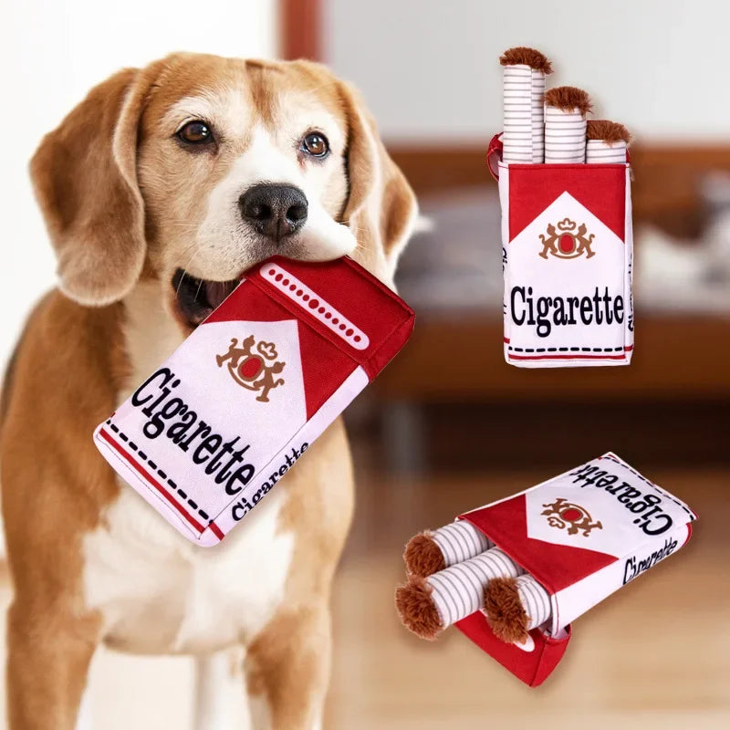 A dog holding a red and white cigarette-themed plush toy for chewing.