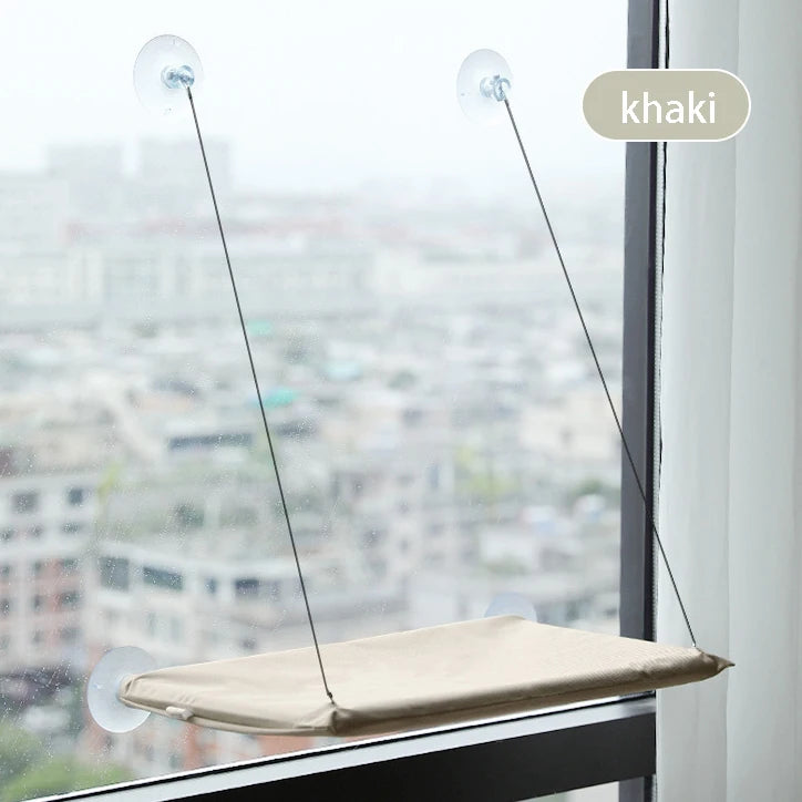 Beige Fenster-Hängematten-Katzenbett, das in einem Fenster hängt und eine Stadtansicht bietet.