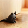 A dark gray cat-shaped door stopper wedge resting on a wooden floor next to a light wood panel.