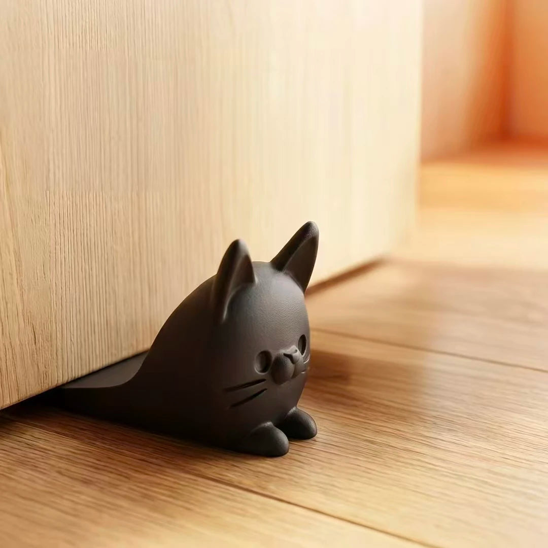 A dark gray cat-shaped door stopper wedge resting on a wooden floor next to a light wood panel.