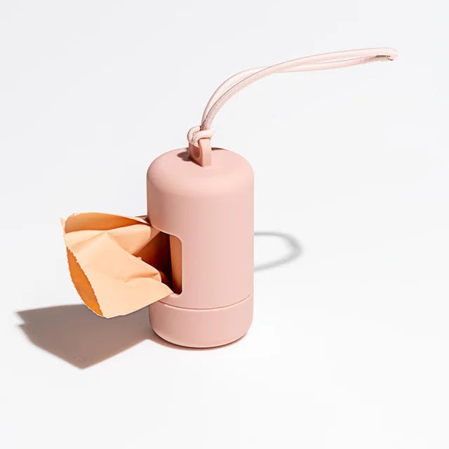 A pink portable dog poop bag dispenser with a light tan bag attached and a loop for carrying.
