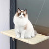 A fluffy blue and white cat is sitting on a beige hanging hammock window perch.