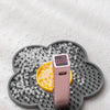 A pink silicone lick mat with a yellow treat is placed on a gray silicone feeding dish.