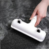 A hand is holding a white reusable pet hair remover brush with suction on a dark surface.