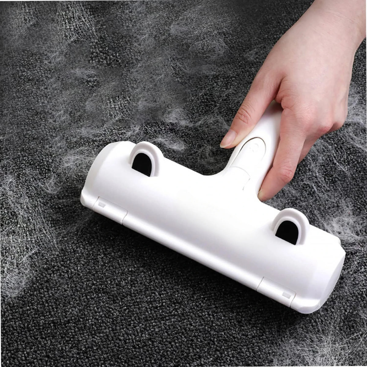A hand is holding a white reusable pet hair remover brush with suction on a dark surface.