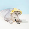 Un gato gris vistiendo un sombrero para orejas ajustable amarillo, acostado sobre una superficie blanca.