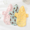 Three pink, teal, and yellow waterproof summer raincoats for dogs displayed on a white surface.