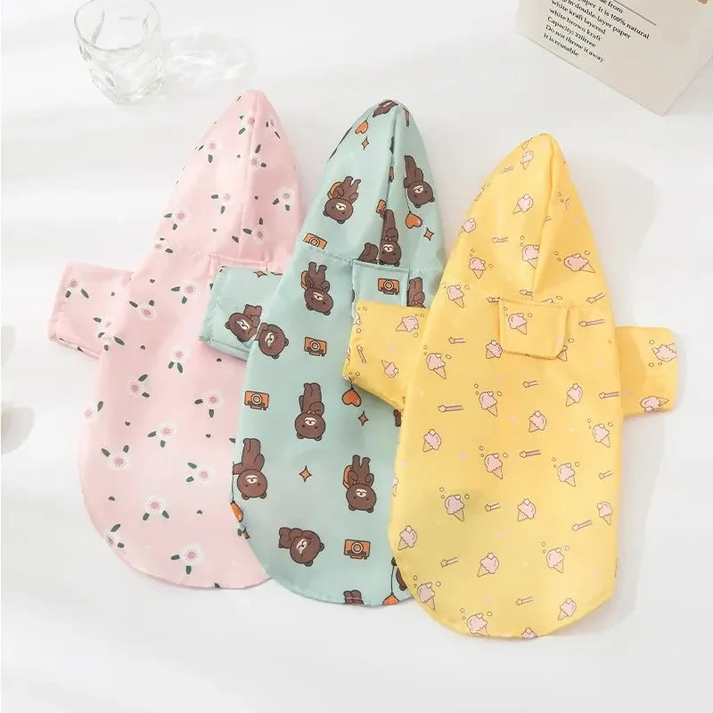 Three pink, teal, and yellow waterproof summer raincoats for dogs displayed on a white surface.