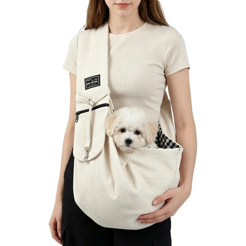 A woman is holding a beige crossbody pet carrier bag designed for dogs and cats.
