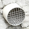 Tapa de rejilla para desagüe de techo redonda y blanca de acero inoxidable contra una pared de piedra rugosa.
