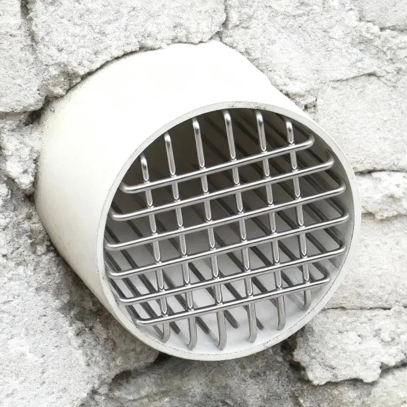 Tapa de rejilla para desagüe de techo redonda y blanca de acero inoxidable contra una pared de piedra rugosa.