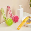 A set of long-handled silicone pet bathing brushes in green and pink next to a white soap dispenser.