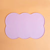 A light purple silicone pet feeding mat with a scalloped edge set against an orange background.
