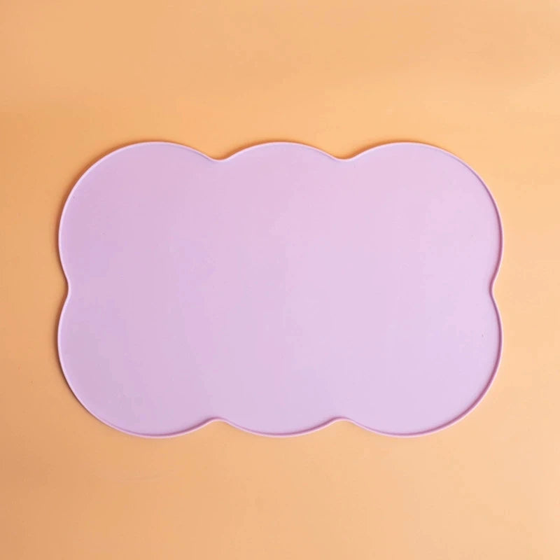 A light purple silicone pet feeding mat with a scalloped edge set against an orange background.