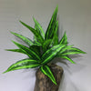A vibrant green artificial tropical palm plant with long, sword-like leaves displayed in a wooden vase.
