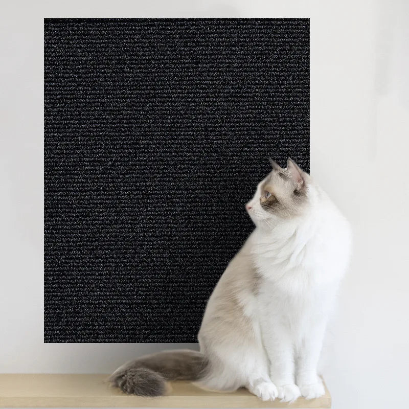 A white and gray cat is sitting on a wooden surface in front of a black textured mat.