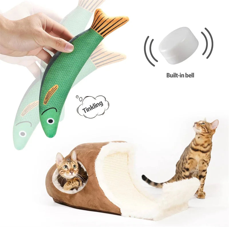 A hand is holding a green plush fish toy with an orange tail, next to a tabby cat.
