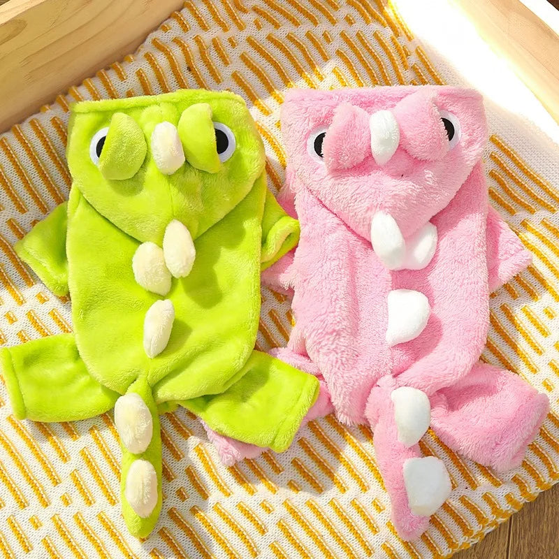 A pair of fuzzy pink and lime green fleece dog hoodies with animal ears lying on a yellow striped fabric.