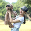 Una joven con gorra de béisbol sostiene a un perro marrón peludo.