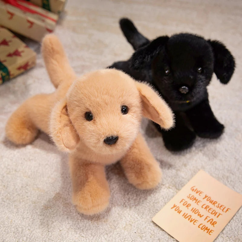 A small, light brown plush dog toy resembling a puppy is lying on a textured surface next to a black dog.