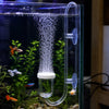 An aquarium CO2 diffuser with a bubble counter and suction cup is shown inside a glass tank surrounded by aquatic plants.