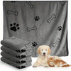 A gray pet bath towel is shown with paw print and bone patterns, next to a stack of folded towels and a cat.