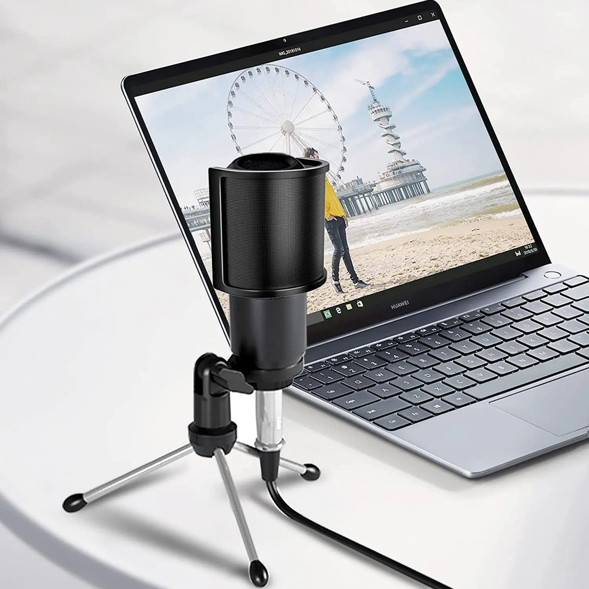 Professioneller Mikrofon-Popfilter und Windschutz, montiert auf einem Stativ neben einem Laptop mit einer Aussicht.